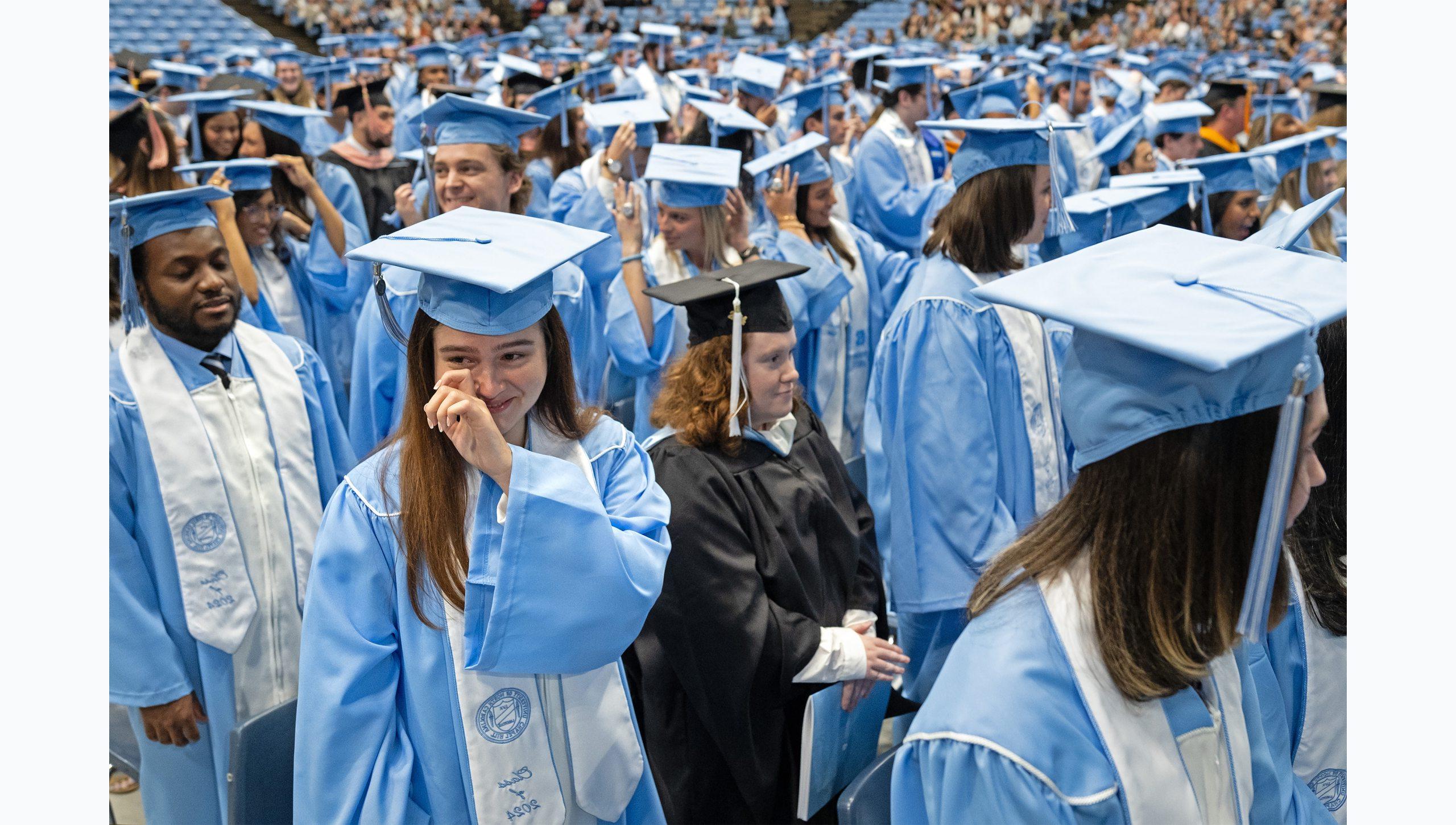 Crowd of graduates at U.N.C. Chapel Hill's Winter Commencement, including one female student wiping away a tear while smiling.